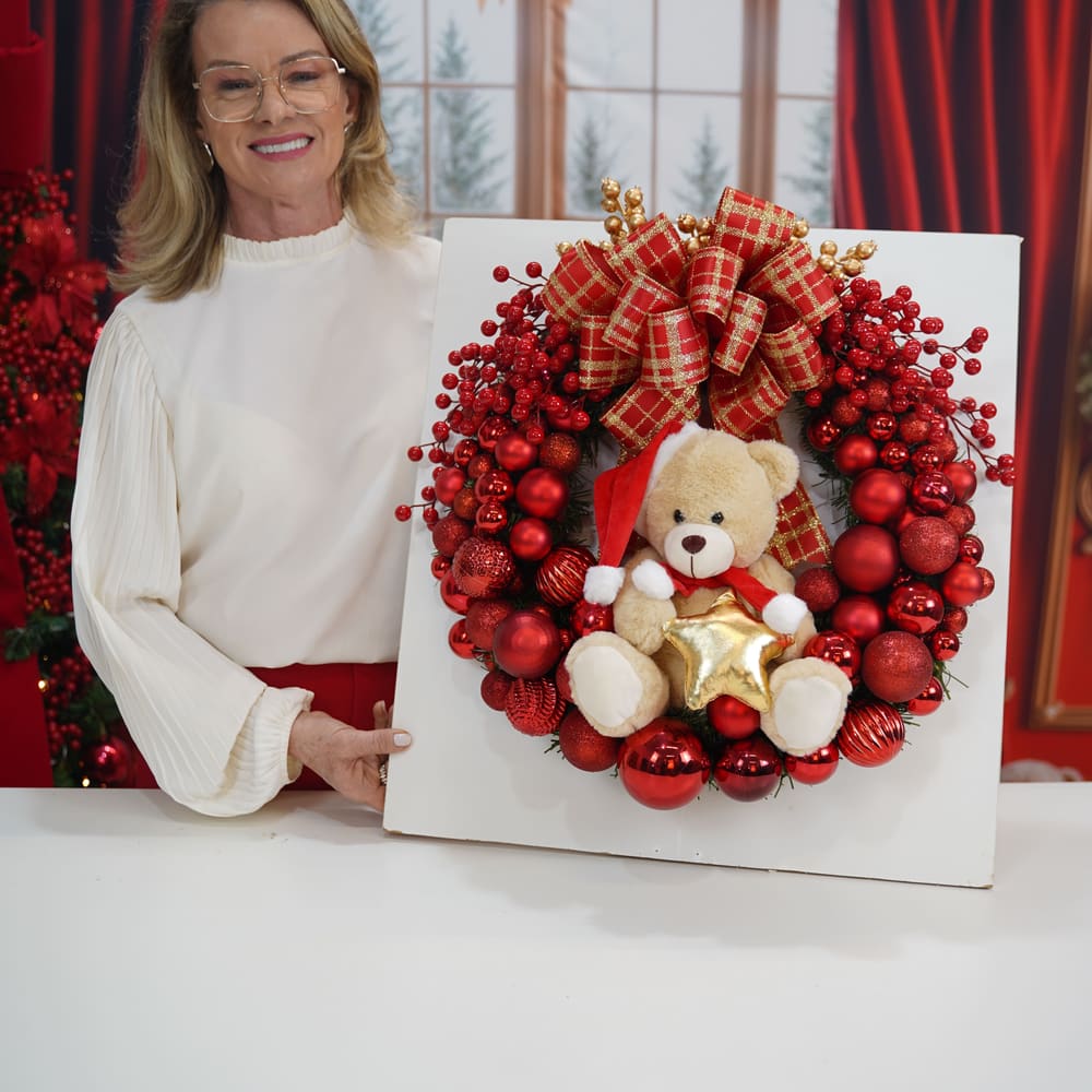 Rose segurando uma guirlanda vermelha com ursinho e estrela dourada.